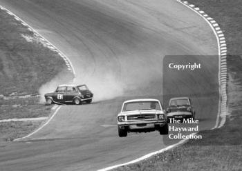 B Thomson, Ford Mustang, and Anita Taylor, Broadspeed Ford Anglia, take the right line as Bill Shaw, Mini Cooper S, investigates the infield at Paddock Bend, British Touring Car Championship Race, Guards International meeting, Brands Hatch 1967.
